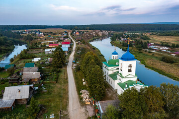 Fototapeta na wymiar View of a Russian village with a spilled river and a beautiful old Orthodox church on shore a birds eye view from a drone