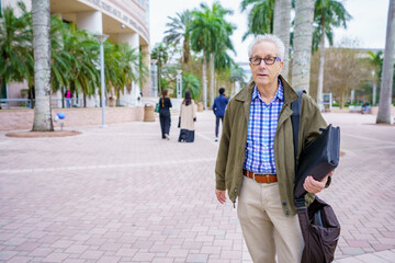 PHoto of a college professor walking on campus with blurry people in background