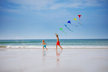 Boys run holding many colorful kite at beach smiling side view