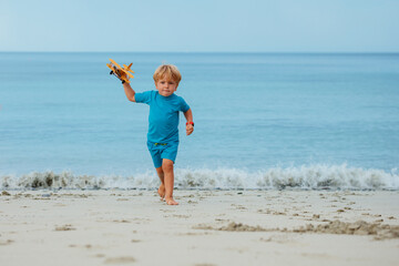 Fototapeta na wymiar Blond boy run with boat toy model at the beach