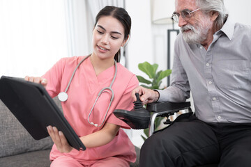 Obraz premium Beautiful nurse take care older caucasian man in electric wheelchair of use tablet computer at home 