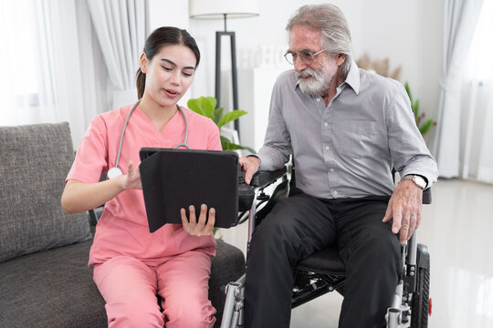 Beautiful Nurse Take Care Older Caucasian Man In Electric Wheelchair Of Use Tablet Computer At Home 