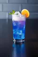 Blue-purple sparkling cocktail with ice and mint and tangerine wedge decoration. Side view, selective focus.