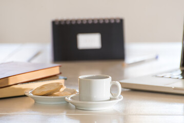 coffee cup and in the background out of focus an agenda, stacked books and a laptop computer.