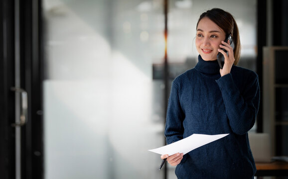 Smiling Businesswoman Using Phone In Office. Small Business Entrepreneur In Casual Wear Standing In Office And Talking On Her Mobile Phone.