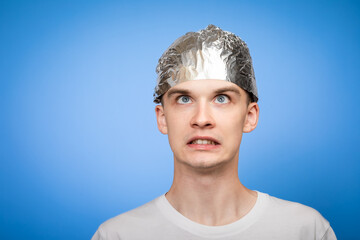 Paranoid young man wearing tin foil hat studio shot on blue background