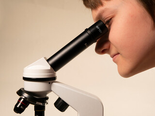 The child looks into the eyepiece of a microscope on a white background. Close-up.