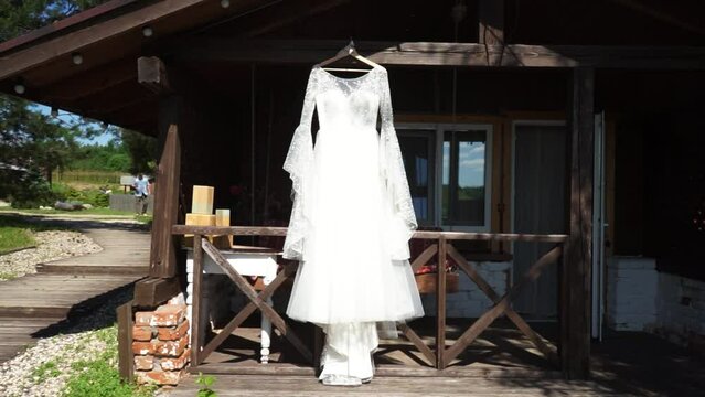 a beautiful white wedding dress hangs on a hanger at the entrance to a wooden house, bungalow