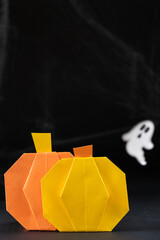 Origami pumpkin made of paper for the Halloween holiday, against the background of flying ghost on a black background, do it yourself.