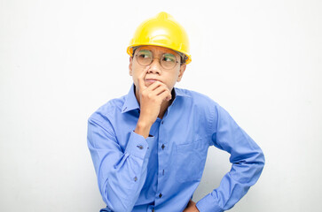 Asian construction worker in blue shirt and yellow safety helmet is seriously thinking with a wondering and thinking gesture and expression.