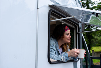 middle-aged woman with cup in hand in motorhome window.con blue shirt and ribbon in hair,
