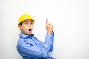 side view of A happy, shocked asian consrtuction worker in blue shirt and yellow safety helmet pointing finger and presenting something ads. 