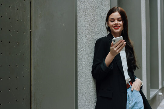 Woman smile with teeth with a phone in her hands walks around the city fashion on the street, spring travel, vacation in the city tourist freelancer, mobile communication and internet for work
