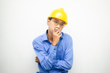 Asian construction worker in blue shirt and yellow safety helmet is seriously thinking with a wondering and thinking gesture and expression.