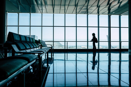 Airport gate and people waiting to fly. Silhouette tourist woman standing and looking outside at the aircrafts. People on vacation or business trip. Travel lifestyle and mirror on the floor. Tourism