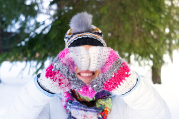 Obraz premium Happiness and joyful outdoor leisure activity people. One woman smiling and doing heart sign gesture with hands wearing warm knitted wool gloves in snow winter holiday vacation travel day concept