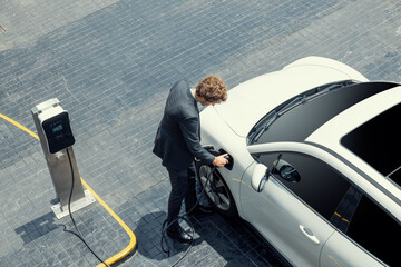 Aerial view of progressive businessman in black formal suit with his electric vehicle recharging...