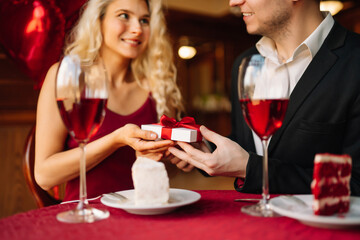 Young couple having a romantic dinner and toasting with glass of red wine. Exchange of gifts. Relationship, surprise and love concept.