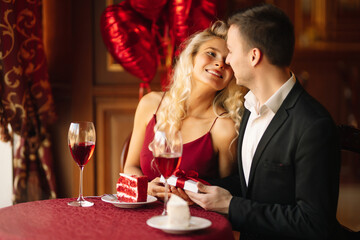 Young couple having a romantic dinner and toasting with glass of red wine. Exchange of gifts. Relationship, surprise and love concept.