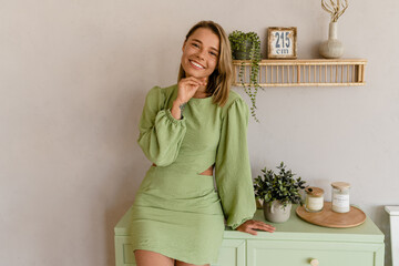 young stylish smiling woman in green summer dress in modern interior apartment home