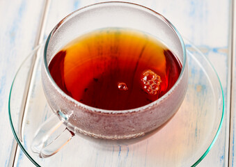 Black tea in a glass mug on a white wooden table.