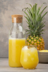 Pineapple juice in a clear glass and bottle on a light table. Pineapple and slices in the background.