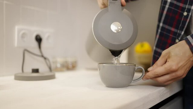 Man pouring water from a kettle into a cup, making tea at home, kitchenware