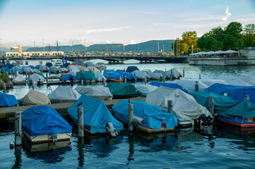 Boats are covered and docked in a bay in Zurich, Switzerland at sunset during the summer