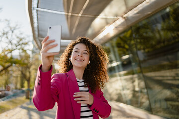 pretty curly woman in city street in stylish pink jacket, student education