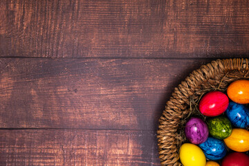 round Easter basket with colorful Easter eggs on brown wooden tabletop, tabletop
