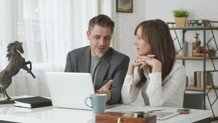 Happy business people working at desk using laptop computer, talking, working together