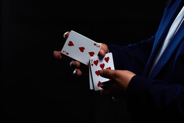 Magician illusionist showing performing card trick. Close up of hand and poker cards on black background.