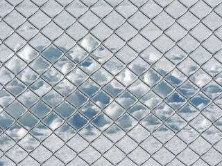 A chain-link fence covered with snow in a sunny winter day