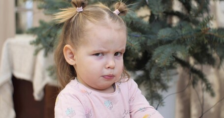 Little cute girl looks at the camera with a funny frown and knitted eyebrows. The child grimaces at the camera with a funny frown. Portrait of cute baby face expression. Funny baby concept.
