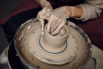 Close-up of a woman beautifully sculpts a brown clay vase on a potter's wheel, a top view