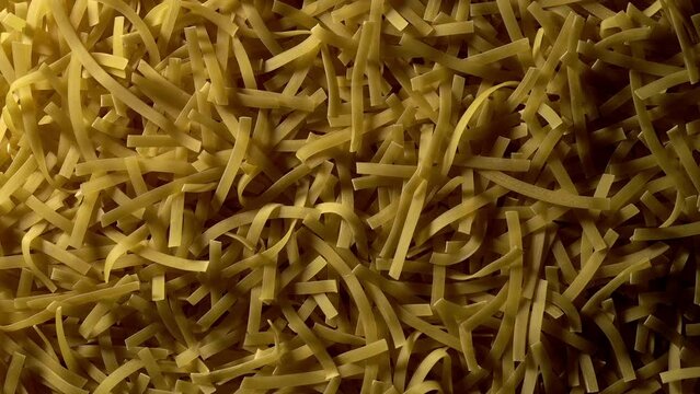 Uncooked Tagliatelle Lungo pasta rotating in slow motion - top view, flat lay, low key, food background. Raw dried organic golden long macaroni texture. Italian food, cuisine and culture close up