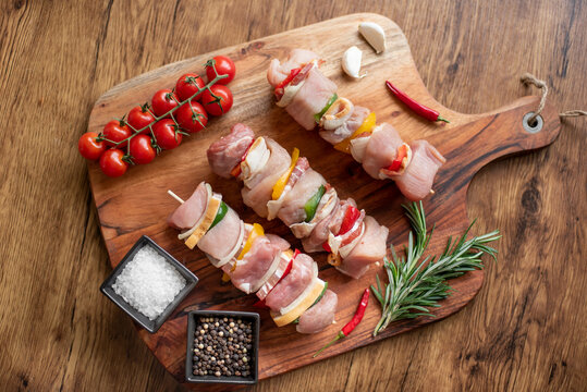 Raw meat skewers with vegetables on wooden background