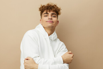 an attractive man stands on a beige background in a white hoodie and looking at the camera smiles pleasantly. Horizontal photo with an empty space for inserting an advertising layout