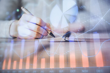 Hands writing information about stock market in notepad. Forex chart holograms in front. Concept of research. Multi exposure