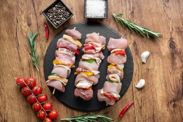 Raw meat skewers with vegetables on wooden background