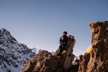 a man sits on a rock against the backdrop of snow-capped mountains with paper cups of coffee