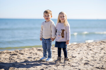 Two toddlers holding hands on the beach - 565706949