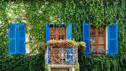 Charming old medieval house with blue shutters, covered with ivy and Virginia creeper. Flowered wrought iron balcony.