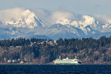 A ferry cross Puget Sound as snow covered Olympic Mountains loom in the background