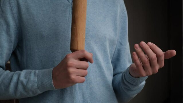 Husband tyrant holds a wooden rolling pin in his hands, close-up. Concept: domestic violence, household choice