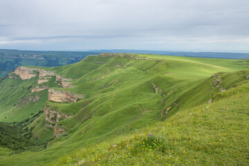Fototapeta na wymiar Panoramic landscape - the Bermamyt plateau in Karachay-Cherkessia with green grass, beautiful hills and the horizon line in a hazy haze and space to copy