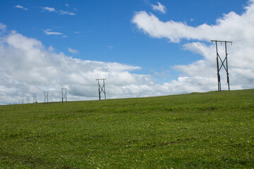 Fototapeta na wymiar Beautiful landscape - electric poles with wires on a boundless green meadow in Karachay-Cherkessia and blue sky with white clouds and space for copying