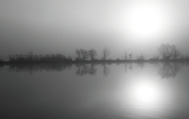 Jezioro we mgle z tłem lasu. Monochrom. Mocna ekspozycja przez światło słoneczne