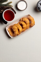mittened hands hold a cardboard plate with donuts. Flatlay on a light background, with a hot drink and fir branches. Vertical