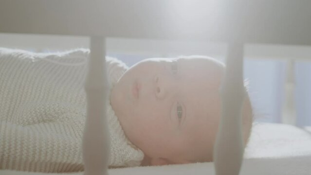 Adorable baby lying in the cradle and looking around while sunlight coming through the window